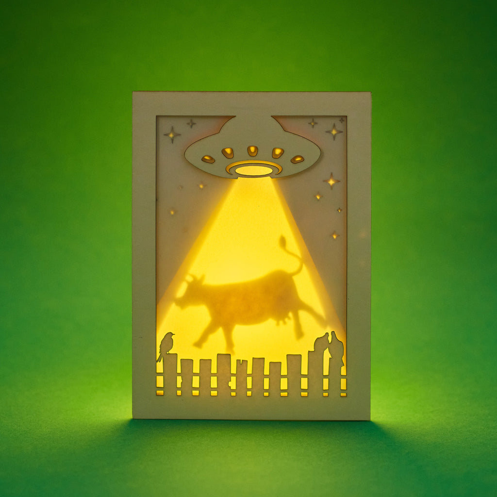 Laser cut shadow box card with a UFO and cow silhouette on a green background