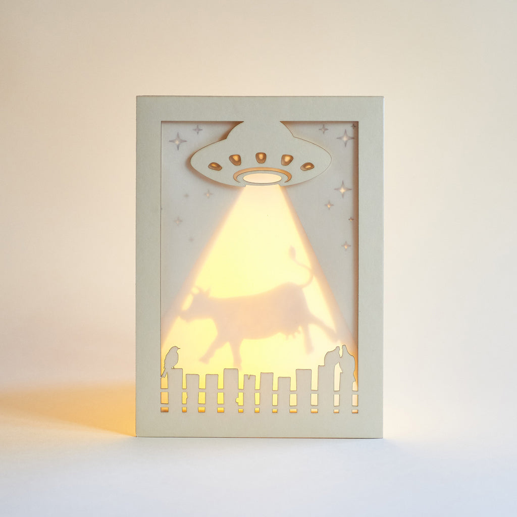 Decorative light greeting card with UFO design casting a warm glow on a plain background