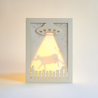 Decorative light greeting card with UFO design casting a warm glow on a plain background