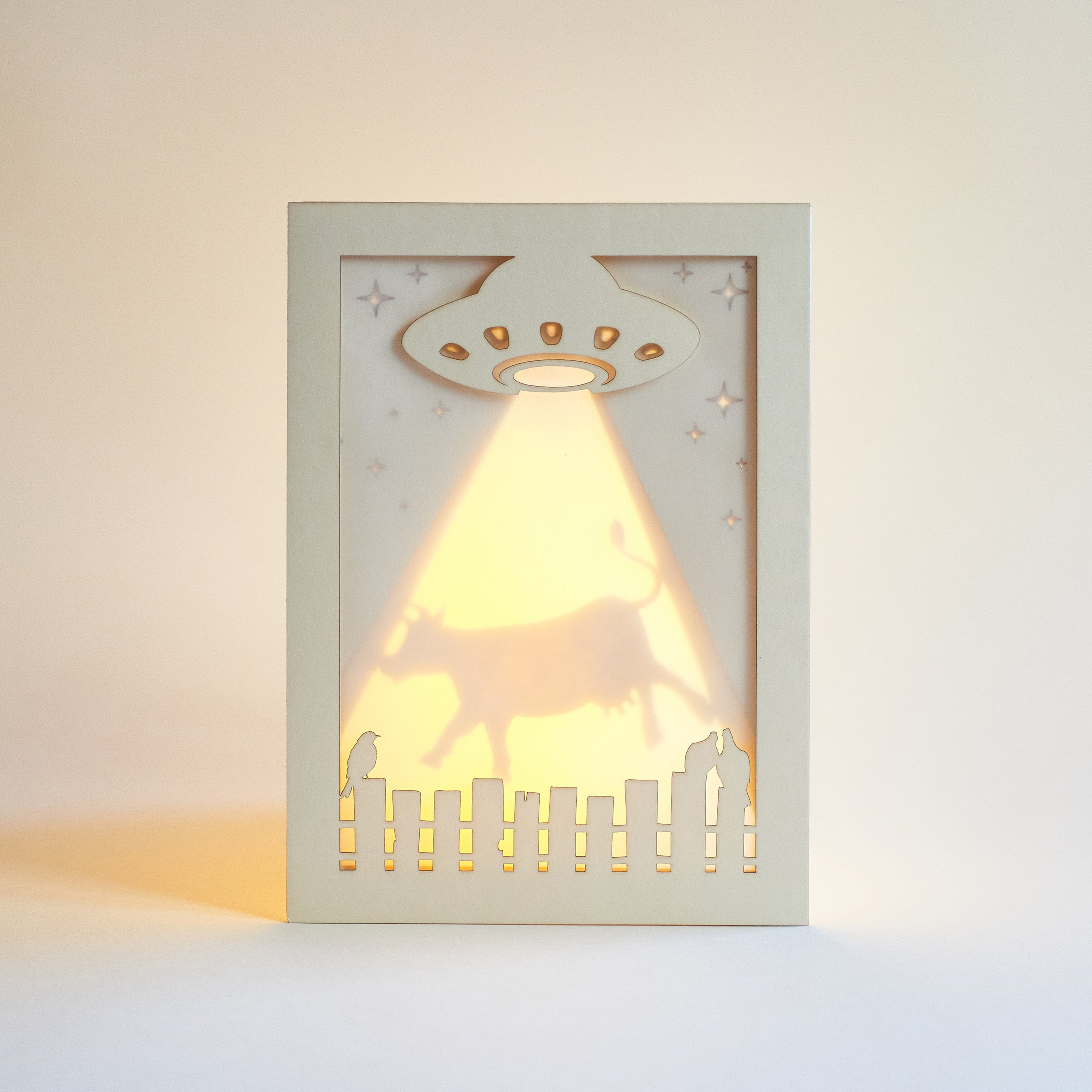 Decorative light greeting card with UFO design casting a warm glow on a plain background