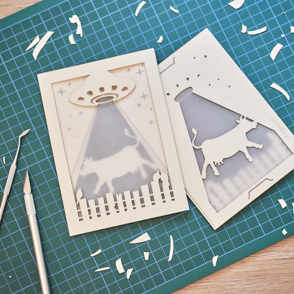 Two laser-cut cards on a green cutting mat with tools.