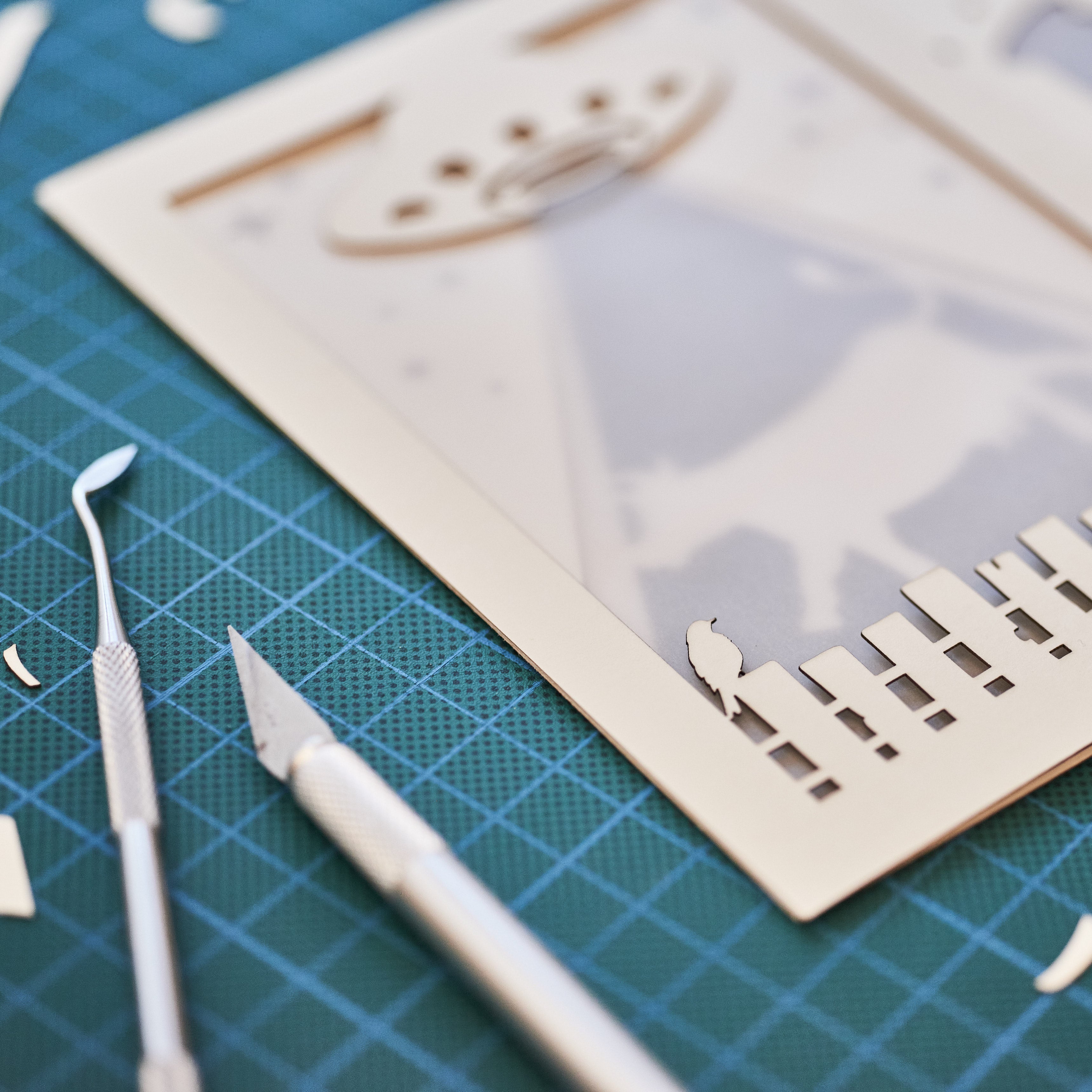 Two laser-cut cards on a green cutting mat with tools.