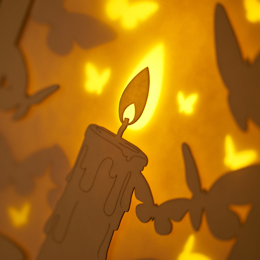 Burning candle with butterflies and moths drawn to flame