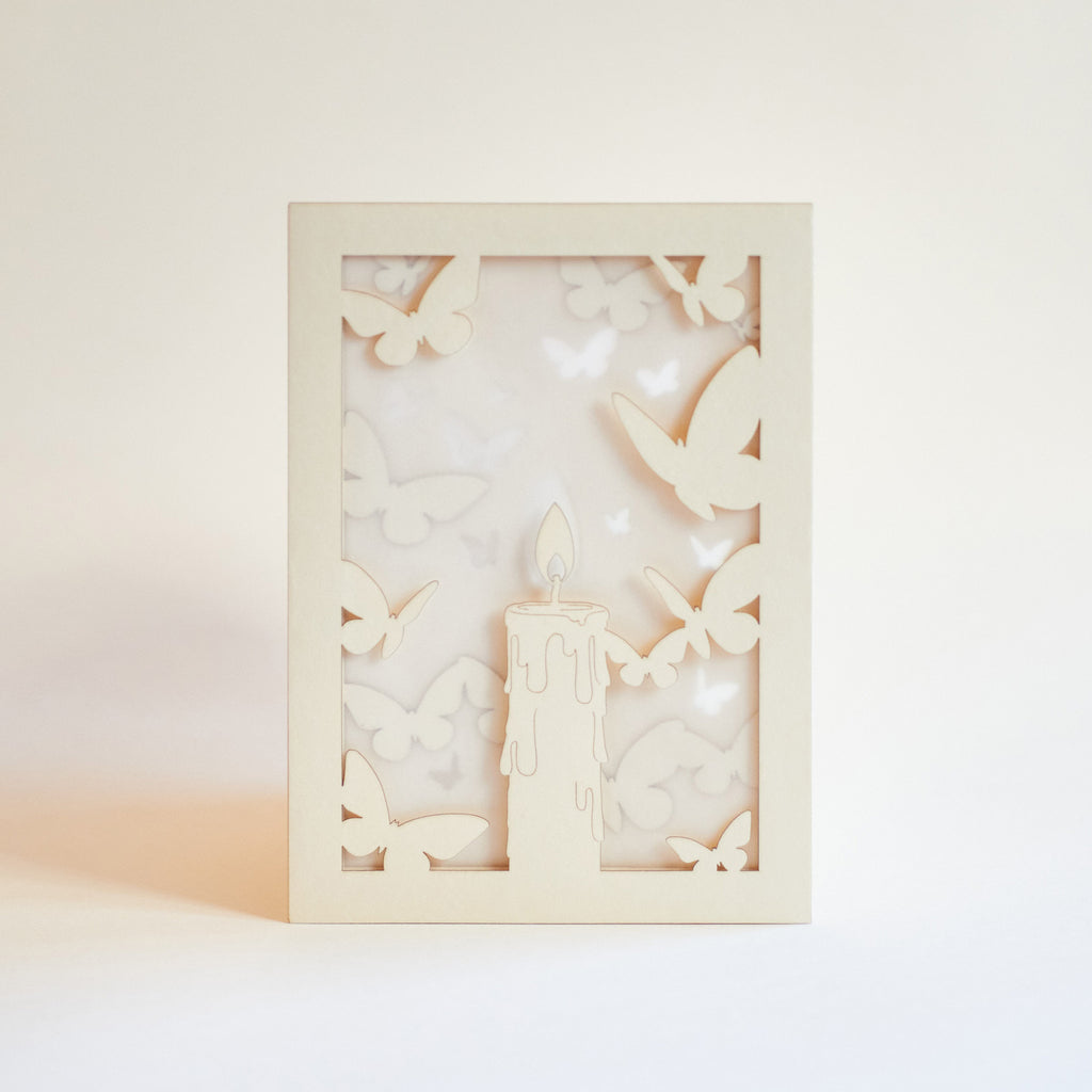 Burning candle with butterflies and moths drawn to flame