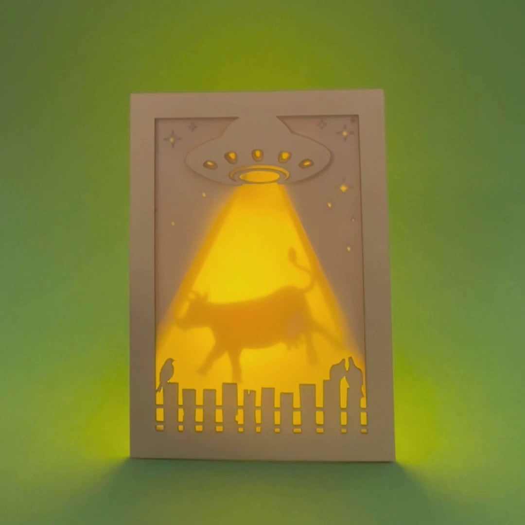 Video of a laser cut shadow box card with a UFO and cow silhouette on a green background